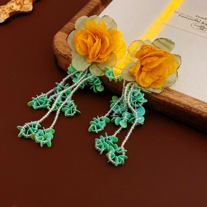 Détail de boucles d'oreilles fleurs en tissu jaune avec glands à paillettes vertes