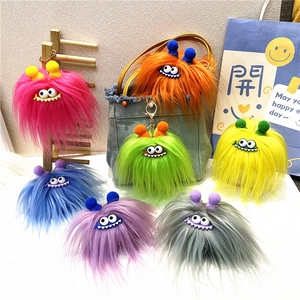 Close-up of colorful plush monster keychains with fuzzy pom-poms on a wooden rack