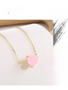 Macro detail of gold necklace with pink stone heart and small cubic zirconia heart pendant