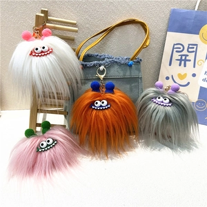 Close-up of fluffy monster keychains in white, orange, grey, and pink with googly eyes