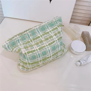 Close-up of green and white tweed makeup bag with elegant woven texture on white desk