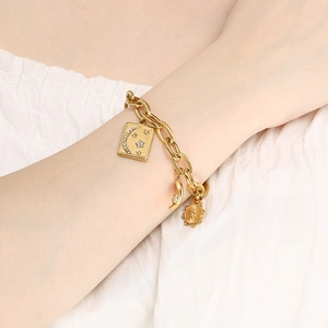 Detailed shot of a gold chain bracelet with star, moon, and sun charms worn on a wrist