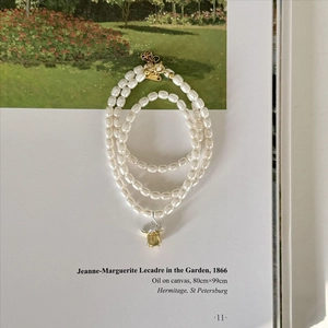 Three-layer pearl necklace with a vintage gold flower bud pendant on an art book
