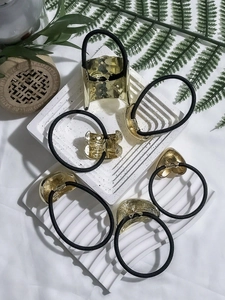 Set of black elastic hair ties with assorted gold metal charms on a white stone display