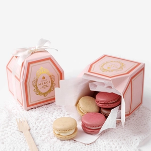 Pink hexagonal paper gift box with gold crown print and macarons on white lace