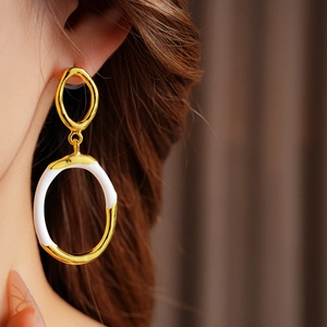 Detail of model wearing gold and white enamel round hoop earrings in soft natural light