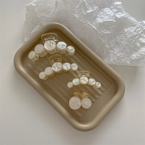 Elegant acrylic pearl claw clips in various sizes displayed on a beige wave tray