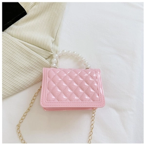 Macro detail of pink quilted handbag featuring pearl handle and golden chain strap