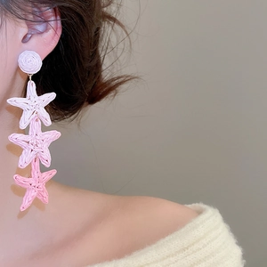 Close-up of pink raffia star tassel earrings with woven texture on a model
