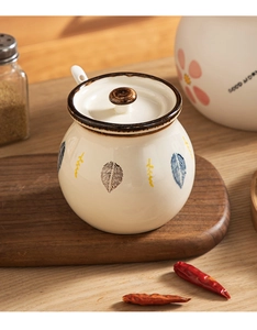 Detailed view of cream ceramic seasoning jar with hand-painted leaves and wooden lid