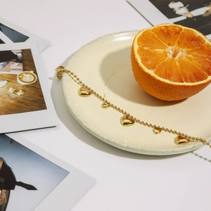 Detailed view of an 18K gold-plated beaded heart bracelet on a ceramic plate with orange