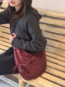 Detail view of red checkered nylon tote bag with decorative side bow on a wooden bench