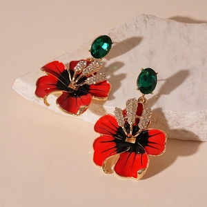 Détail de boucles d'oreilles fleur en émail rouge avec pierre verte et cristaux brillants