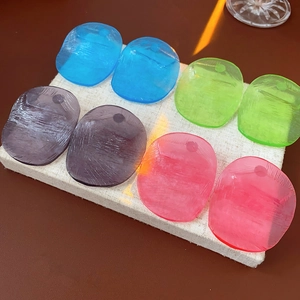 Detail of colorful resin earrings with ice crack texture on a beige linen mat