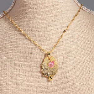 Detail of gold-plated cloud pendant with pink teardrop gemstone on beige mannequin