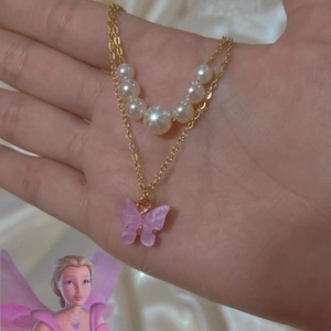Close-up of golden double-layer necklace with white pearls and purple butterfly charm