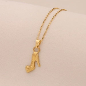 Gros plan d'un collier en acier inoxydable doré avec pendentif botte sur fond beige