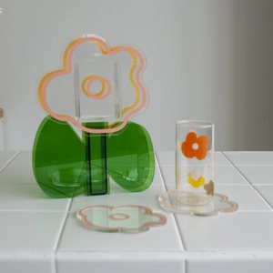 Floral acrylic coaster and vase set with glass cup on a minimalist white countertop