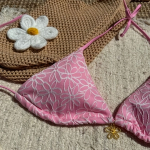 Detail of pink bikini top with white floral embroidery and a gold flower charm
