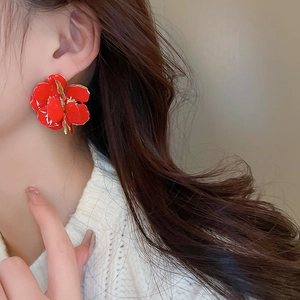 Detail of red floral enamel earring with gold edges worn by a model in soft lighting