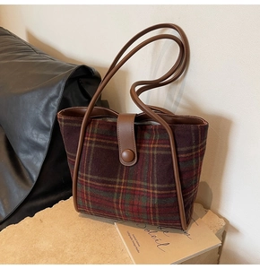 Detail of vintage plaid woolen tote bag with brown PU leather handles on a stone pedestal