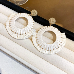Detail of white raffia flower drop earrings with golden beads on a soft velvet display