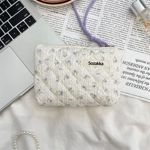 Quilted floral cotton pouch with top zipper and woven label on a lifestyle desk background