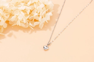 Silver heart pendant necklace with polished finish on a minimalist orange background