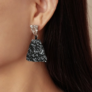 Close-up of asymmetric geometric earrings showing silver and black wrinkled metal texture