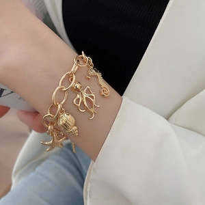 Detail of golden ocean charm bracelet with starfish and shell pendants on wrist