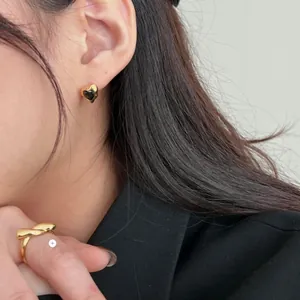 Detail of heart stud earrings with black stone and gold twist ring on a model