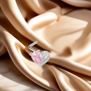 Macro shot of L-shaped nose stud with pink heart zircon and silver wing on silk fabric