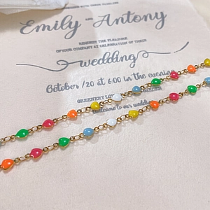 Détail d'un collier chaîne dorée avec des perles en cœur colorées sur papier crème