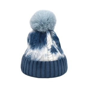 Close-up of tie-dye knit beanie with cable patterns and a faux fur pompom detail