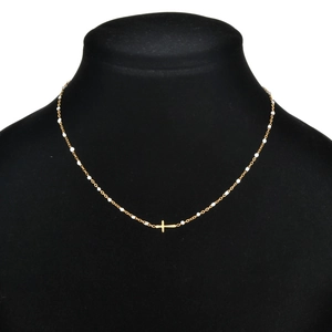Detail of gold cross pendant necklace with white enamel beads on black jewelry bust