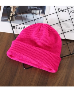 Close-up of rose red ribbed knit beanie on a rustic wood surface with artistic background