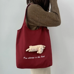 Detail of burgundy canvas tote bag featuring a 3D plush cat charm and white embroidery