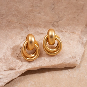 Gros plan détaillé de boucles d'oreilles anneaux entrelacés en métal doré mat
