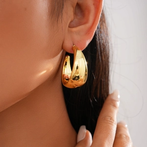 Close-up of a chunky gold hoop earring worn by a model in natural warm lighting
