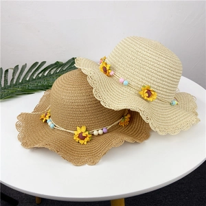Detail of children's straw hats with wavy brims, featuring yellow sunflower accents