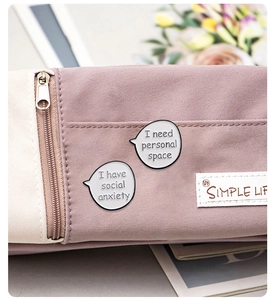 Detail view of round enamel pins with social anxiety text on a canvas bag accessory