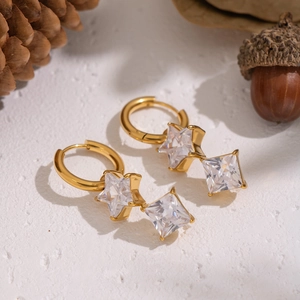 Detail of gold-plated star drop earrings with white zircons on a rustic backdrop