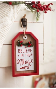 Close-up of a Christmas wooden sign with red berries and Believe in the Magic text