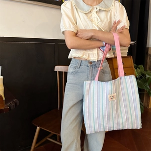 Dettaglio di una borsa tote in tela a righe con manici rosa in ambiente interno
