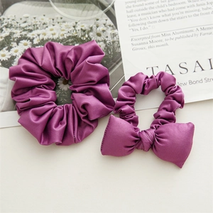 Close-up of two purple satin hair scrunchies with elastic bow detail on magazine background