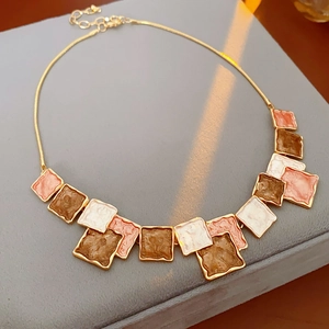 Close-up of golden necklace with colorful square enamel tiles on a gray velvet jewelry box