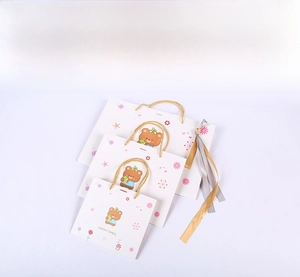 Detailed view of three sizes of white cartoon bear gift bags with gold handles and ribbons