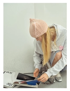 Pink chunky knit cat ear beanie with bow detailing worn by a model in a stylish pose