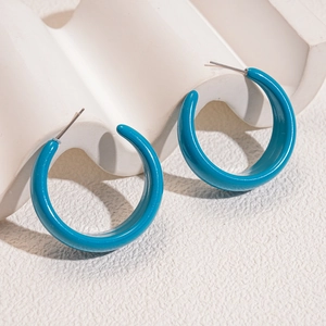 Minimalist teal blue C-shaped hoop earrings with polished finish on wavy white podium