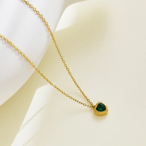 Macro shot of gold-plated necklace featuring a green heart-shaped zircon pendant